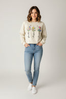 Beige sweatshirt with floral designs and text 'faith', 'hope', 'love' on a wooden surface.