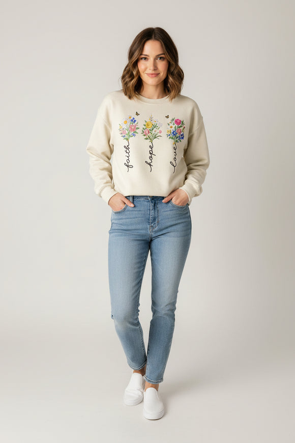 Beige sweatshirt with floral designs and text 'faith', 'hope', 'love' on a wooden surface.