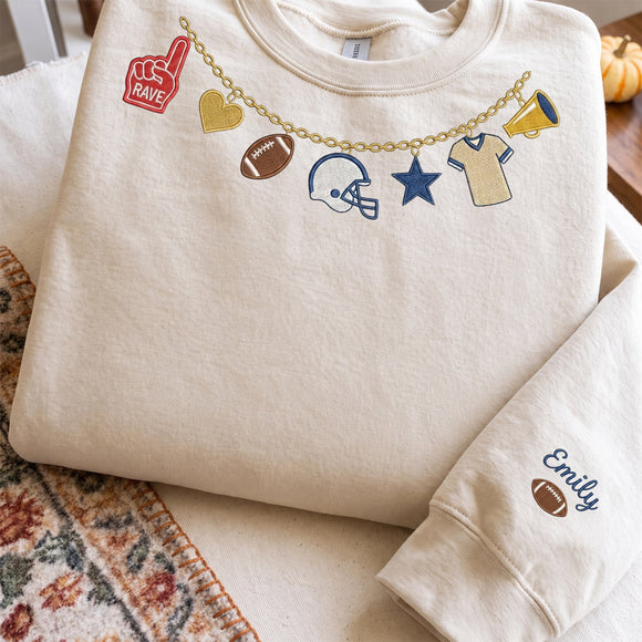 Cream embroidered sweatshirt featuring a game day football charm necklace neckline design and customized name on sleeve cuff.