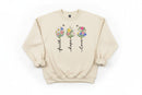 Beige sweatshirt with floral designs and text 'faith', 'hope', 'love' on a wooden surface.