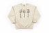 Beige sweatshirt with floral designs and text 'faith', 'hope', 'love' on a wooden surface.