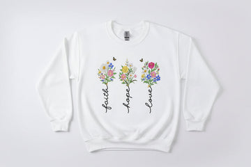 White sweatshirt with floral designs and text 'Faith', 'Hope', 'Love' on a white background.