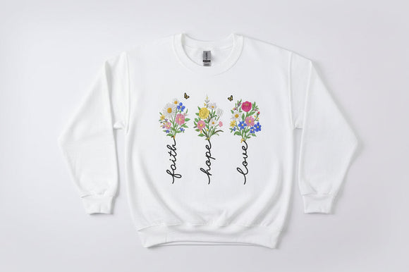 White sweatshirt with floral designs and text 'Faith', 'Hope', 'Love' on a white background.