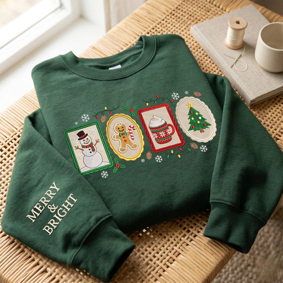A dark green crewneck sweatshirt with festive Christmas graphics, laid flat on a woven wicker table. The sweatshirt features four embroidered holiday-themed panels (a snowman, a gingerbread man, a mug of hot cocoa, and a Christmas tree) across the chest, 'MERRY & BRIGHT' embroidered in gold on the left sleeve, and is styled next to a spool of thread and a ceramic mug.