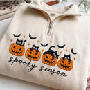 Cream-colored quarter-zip sweatshirt featuring embroidered Halloween graphics with four jack-o'-lanterns, black cats, bats, stars, and the text 'spooky season'.