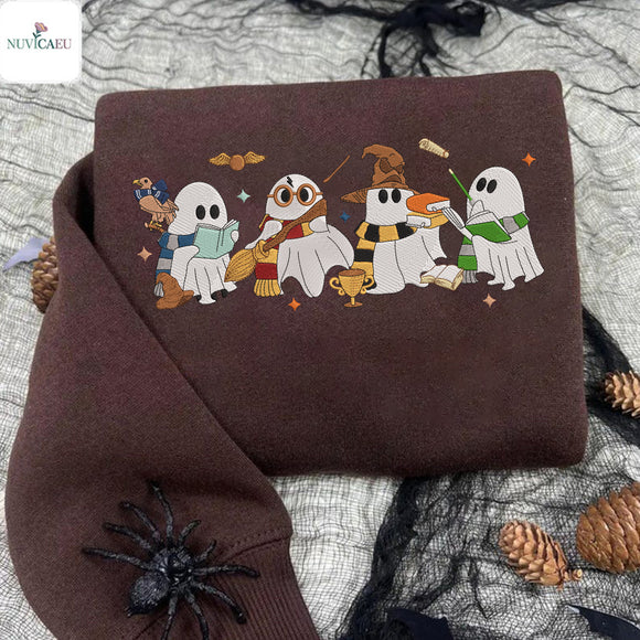 A folded brown sweatshirt with a colorful graphic of four cartoon ghosts dressed as wizards, displayed on a gray fabric background with black spiderwebs, pinecones, and a black spider decoration.